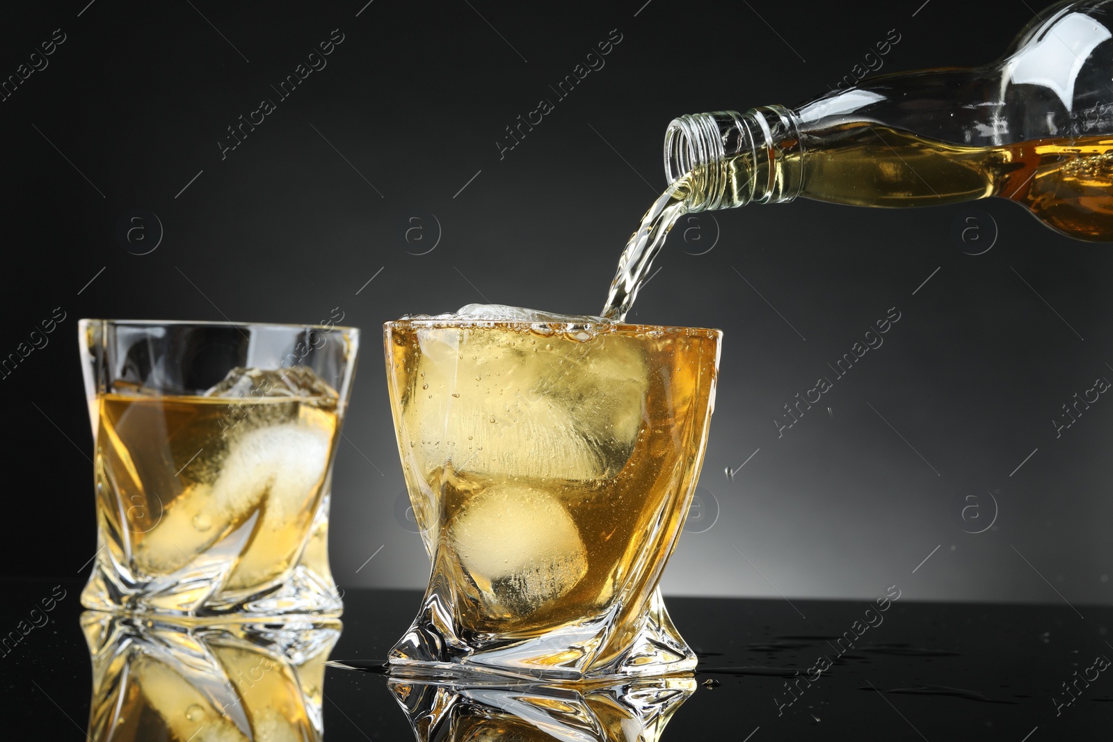 Photo of Pouring tasty whiskey from bottle into glass at mirror table, closeup