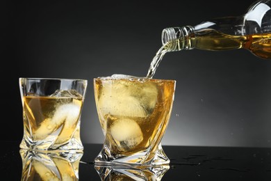 Photo of Pouring tasty whiskey from bottle into glass at mirror table, closeup