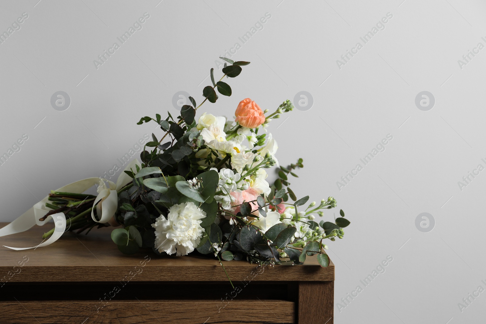 Photo of Bouquet of beautiful flowers on wooden table against white wall. Space for text