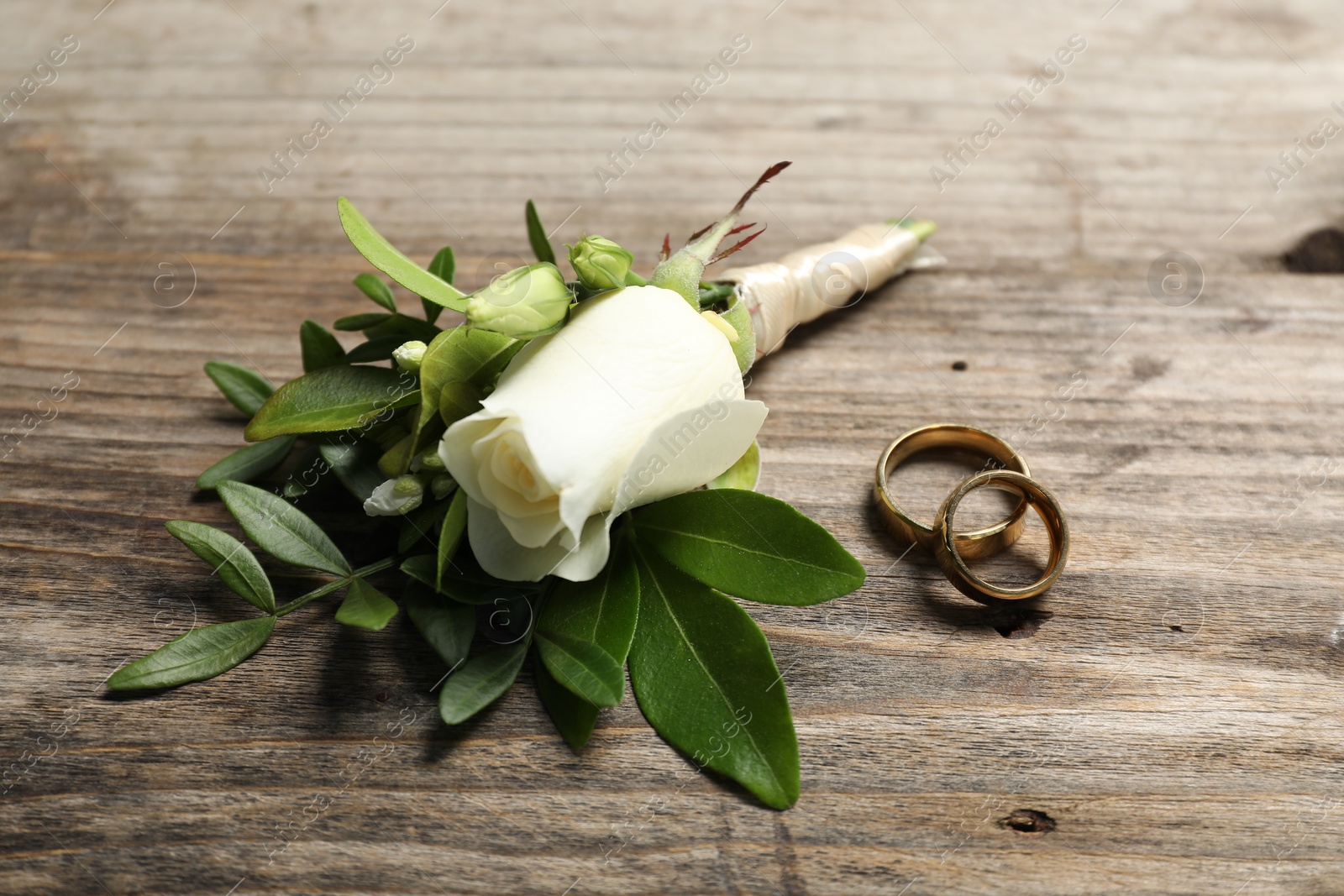 Photo of Wedding stuff. Stylish boutonniere and rings on wooden table, closeup
