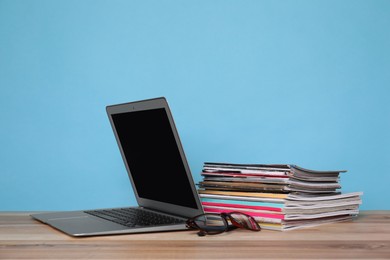 Photo of Laptop, glasses and stack of magazines on wooden table