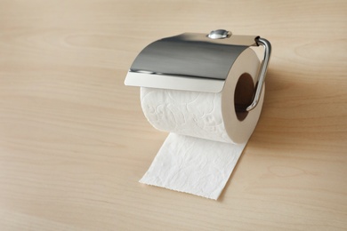 Photo of Holder with toilet paper roll on wooden background