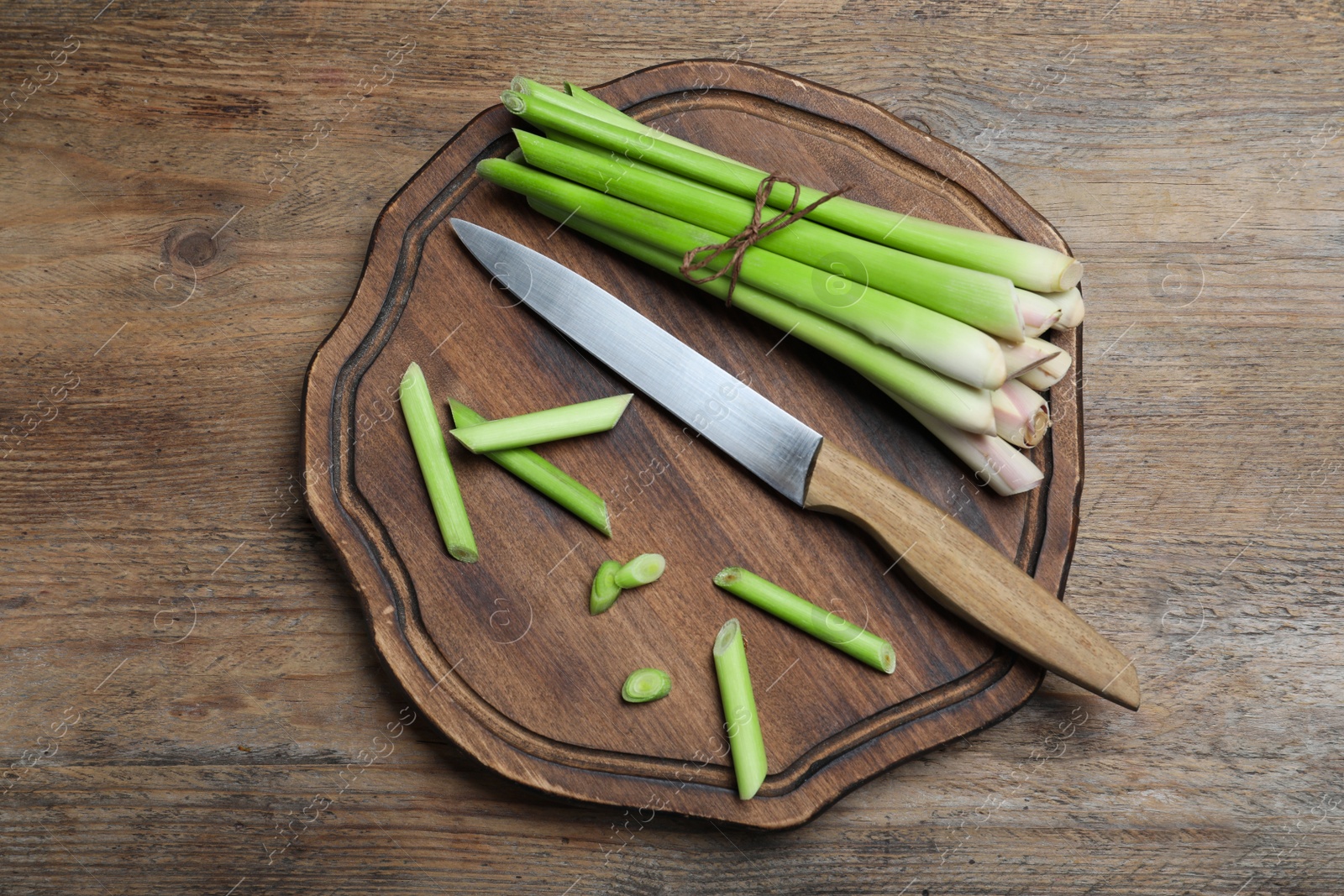 Photo of Fresh lemongrass, knife and cutting board on wooden table, top view