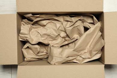 Photo of One open cardboard box with crumpled paper on white wooden floor, top view