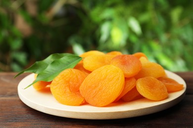 Photo of Plate of tasty apricots on wooden table against blurred green background. Dried fruits