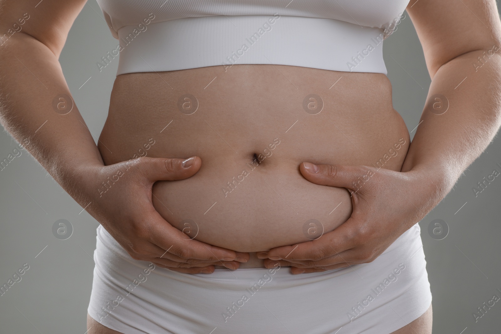 Photo of Woman touching belly fat on grey background, closeup. Overweight problem