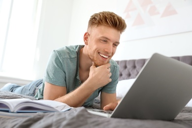 Young man using laptop while lying on bed at home