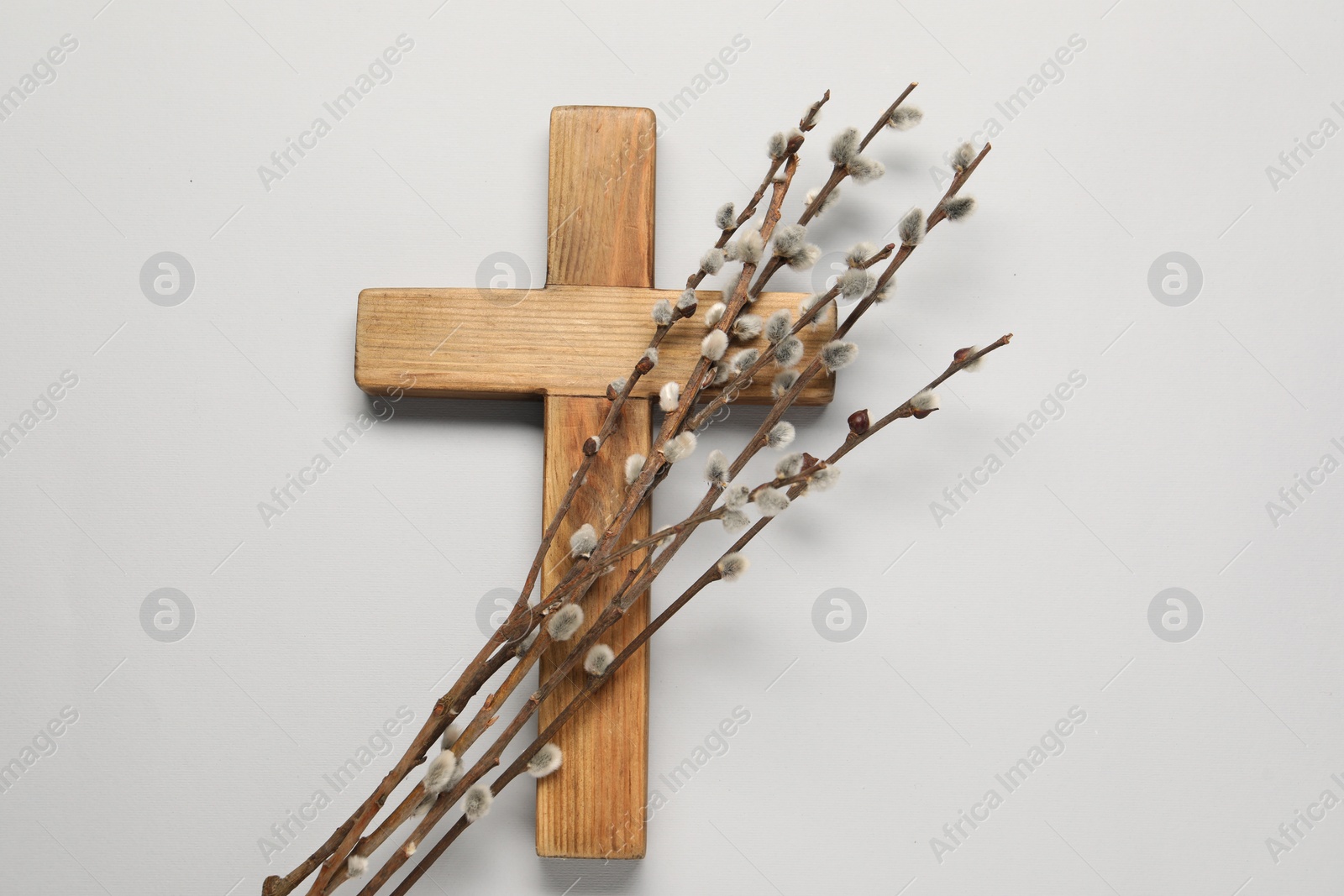 Photo of Wooden cross and willow branches on light grey background, top view. Easter attributes