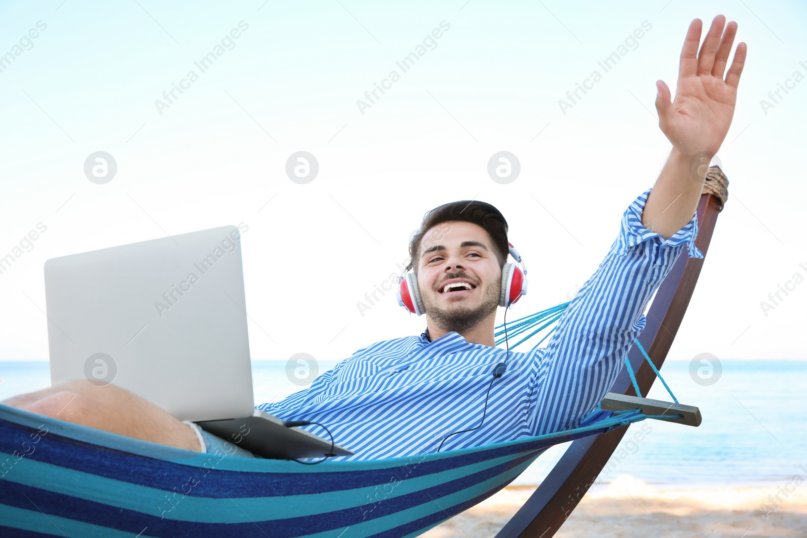 Photo of Young man listening to music in comfortable hammock at seaside