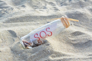 Photo of Glass bottle with seashells and message SOS on sand