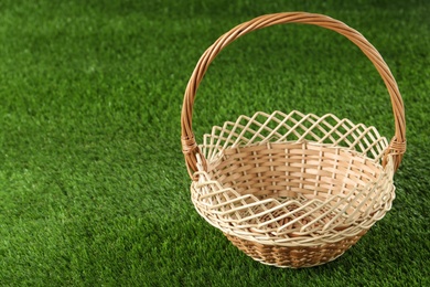 Empty wicker basket on green lawn, space for text. Easter item