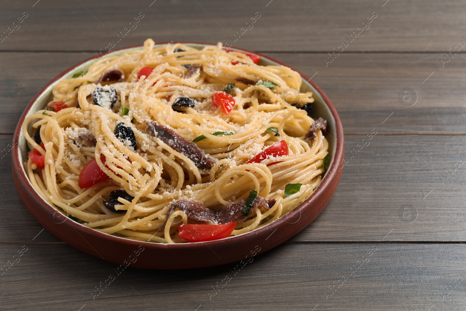 Photo of Plate of delicious pasta with anchovies, tomatoes and parmesan cheese on wooden table