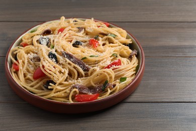 Plate of delicious pasta with anchovies, tomatoes and parmesan cheese on wooden table