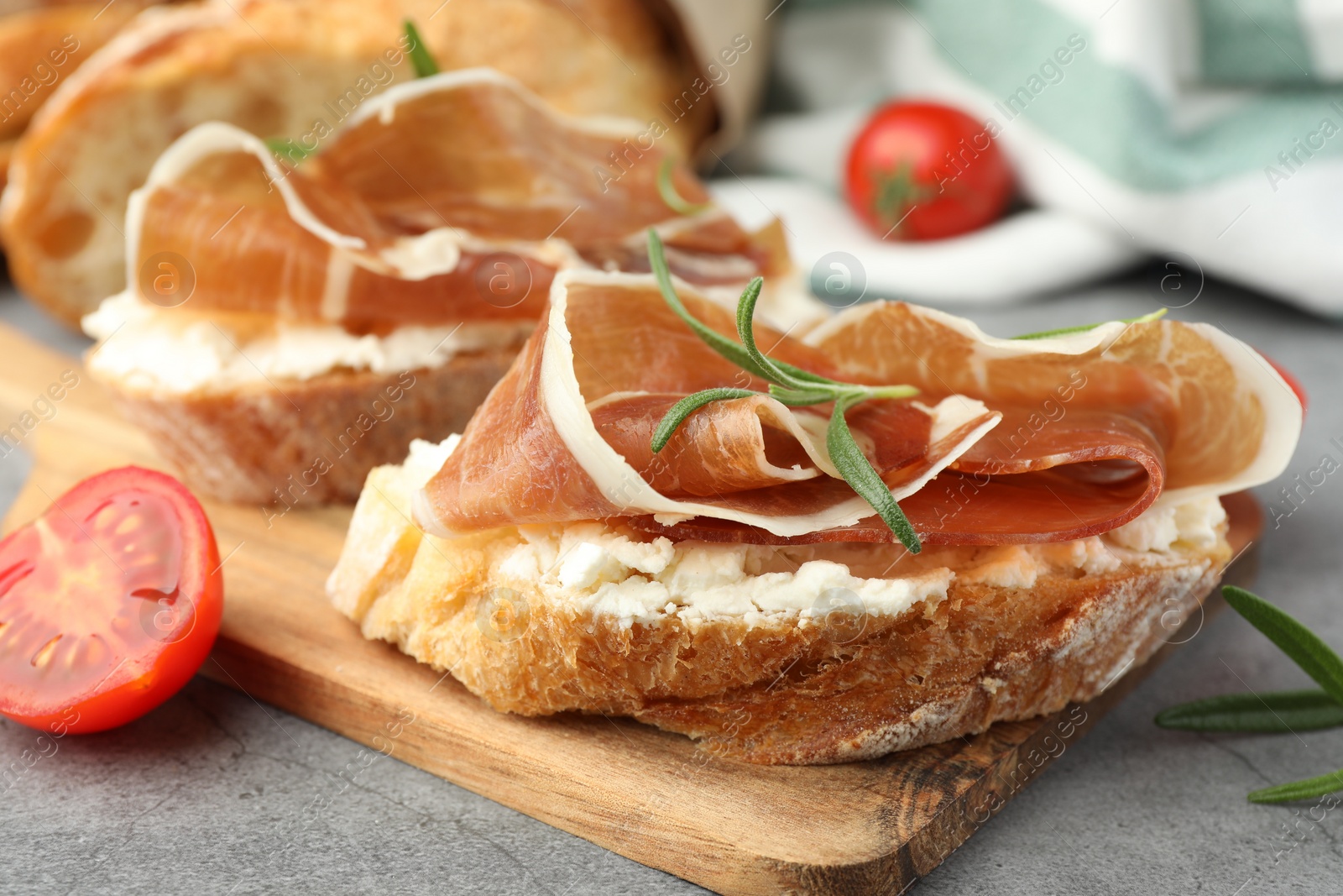 Photo of Tasty sandwiches with cured ham, tomatoes and rosemary on grey table, closeup