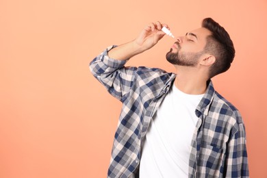 Photo of Man using nasal spray on peach background, space for text