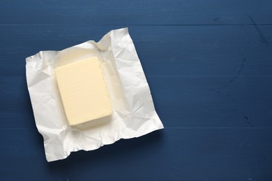 Photo of Block of tasty butter in open foil packaging on blue wooden table, top view. Space for text