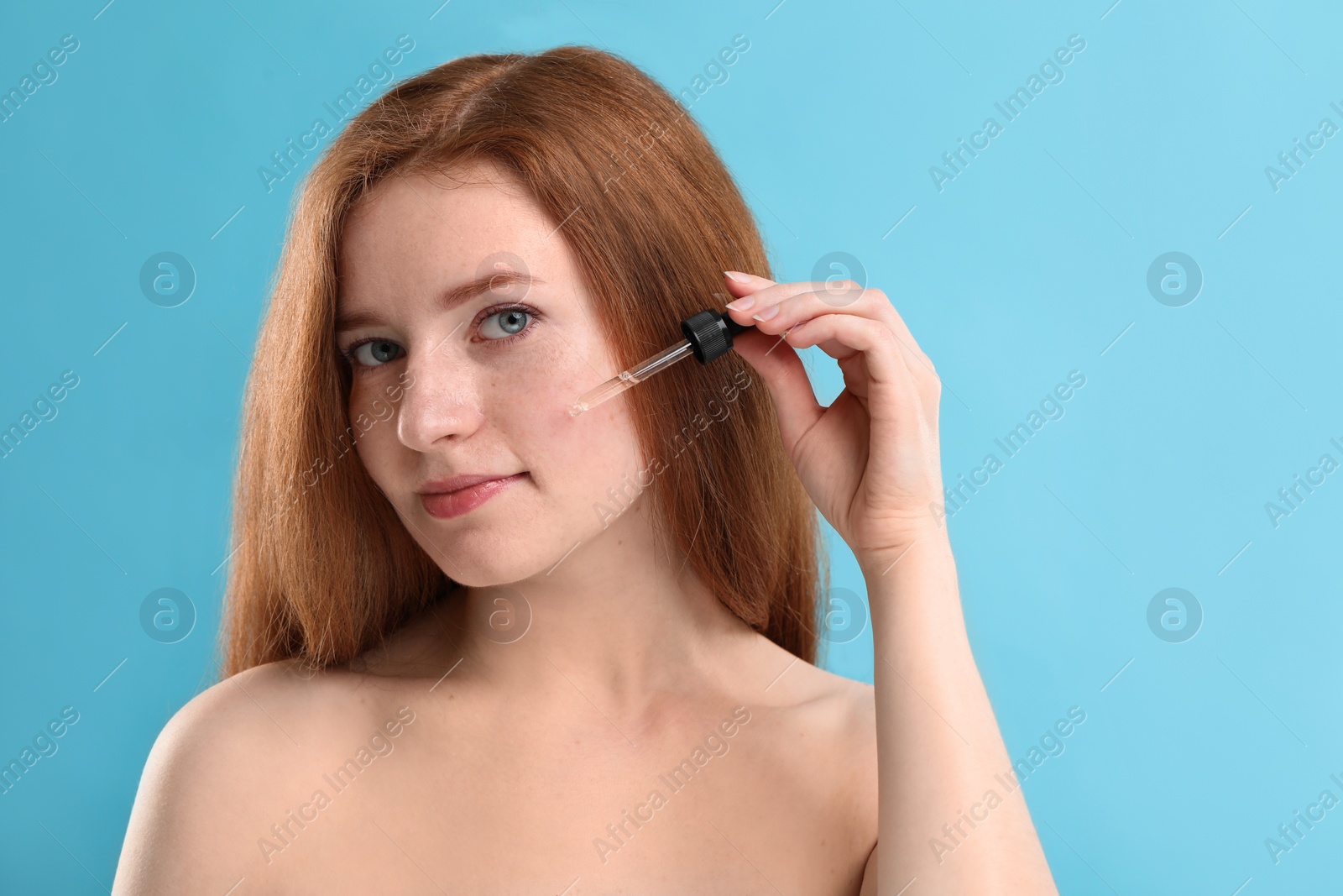Photo of Beautiful woman with freckles applying cosmetic serum onto her face against light blue background. Space for text