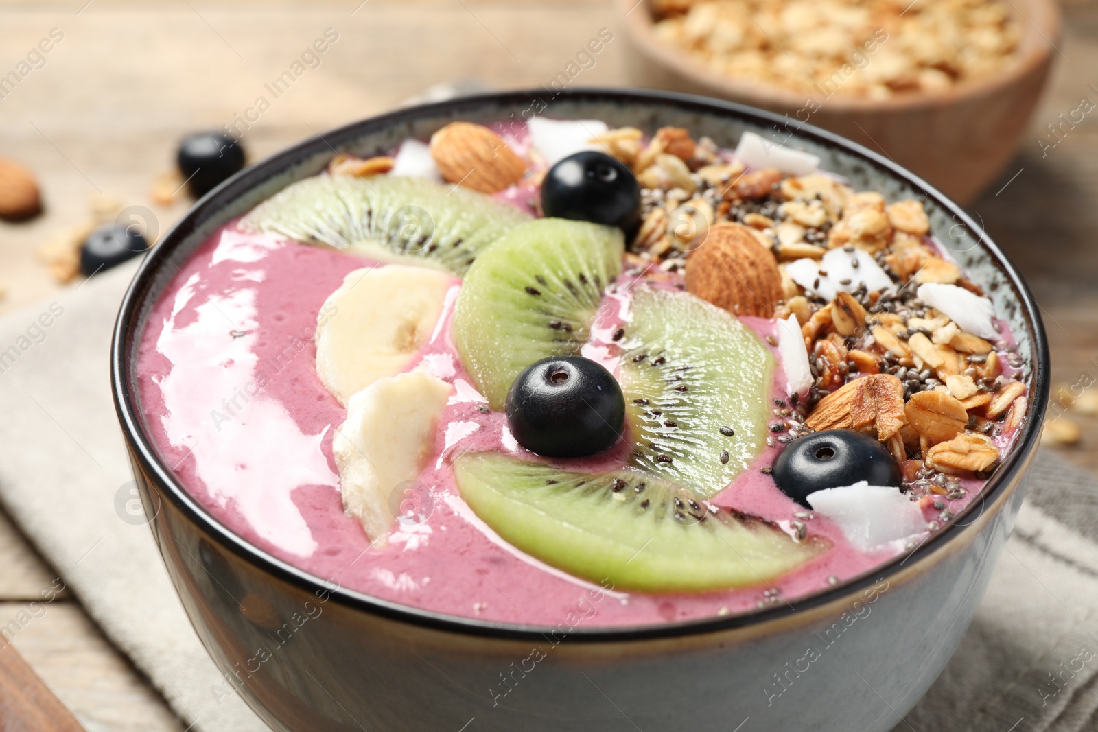 Photo of Delicious acai smoothie with granola and fruits in dessert bowl on table, closeup