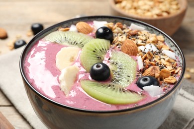 Photo of Delicious acai smoothie with granola and fruits in dessert bowl on table, closeup