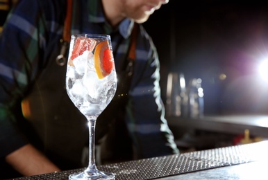 Photo of Barman with grapefruit gin tonic cocktail at counter in pub, closeup. Space for text