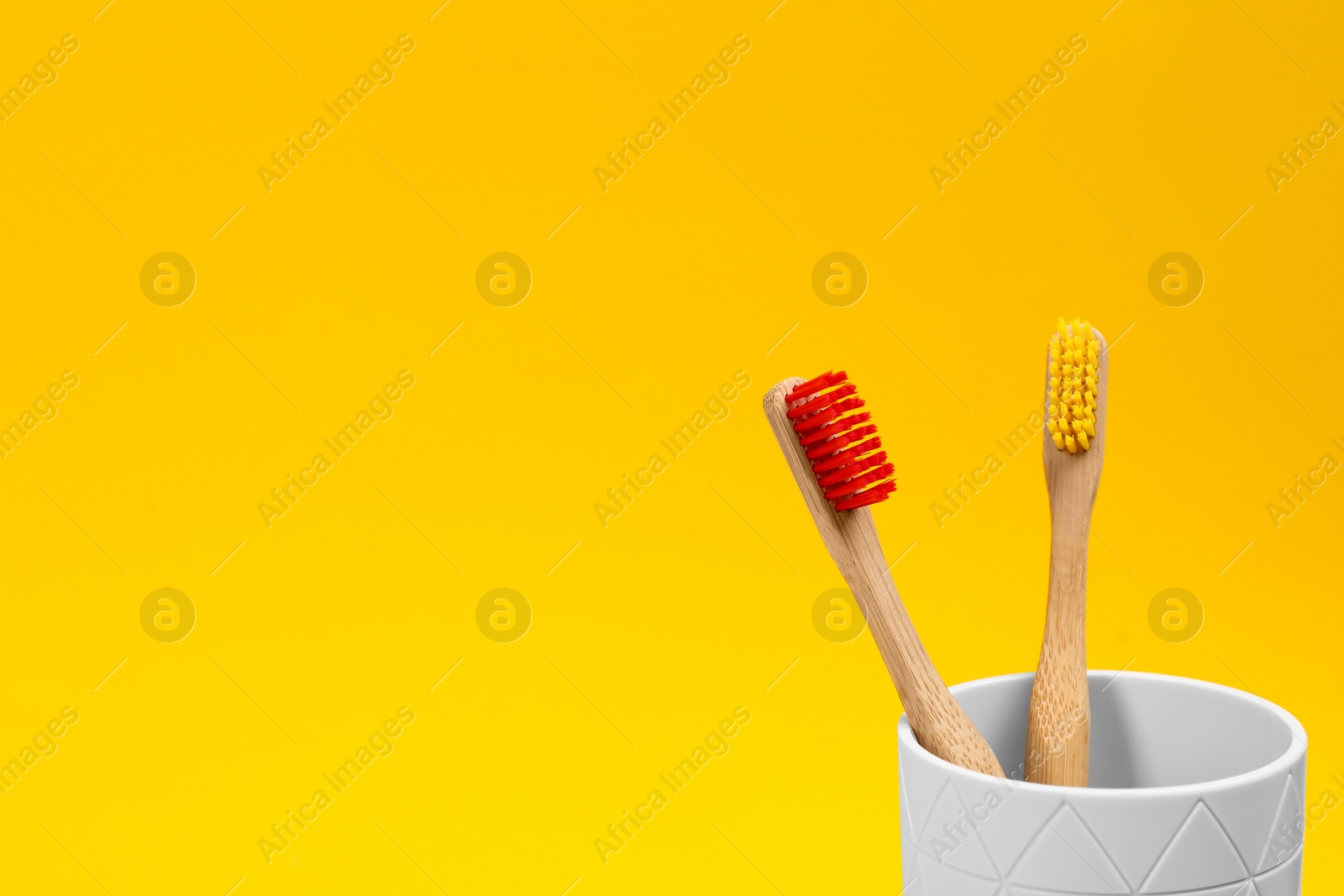 Photo of Toothbrushes made of bamboo in holder on yellow background. Space for text