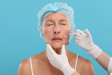 Photo of Doctor giving lips injection to senior woman on light blue background. Cosmetic surgery