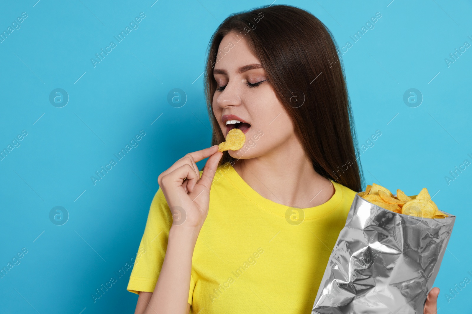 Photo of Pretty young woman eating tasty potato chips on light blue background
