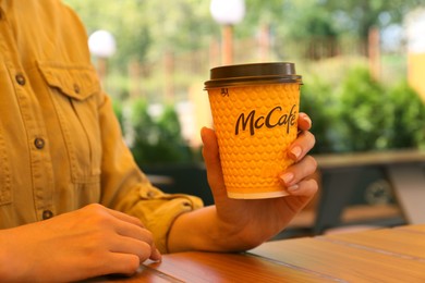 MYKOLAIV, UKRAINE - AUGUST 11, 2021: Woman with hot McDonald's drink in outdoor cafe, closeup