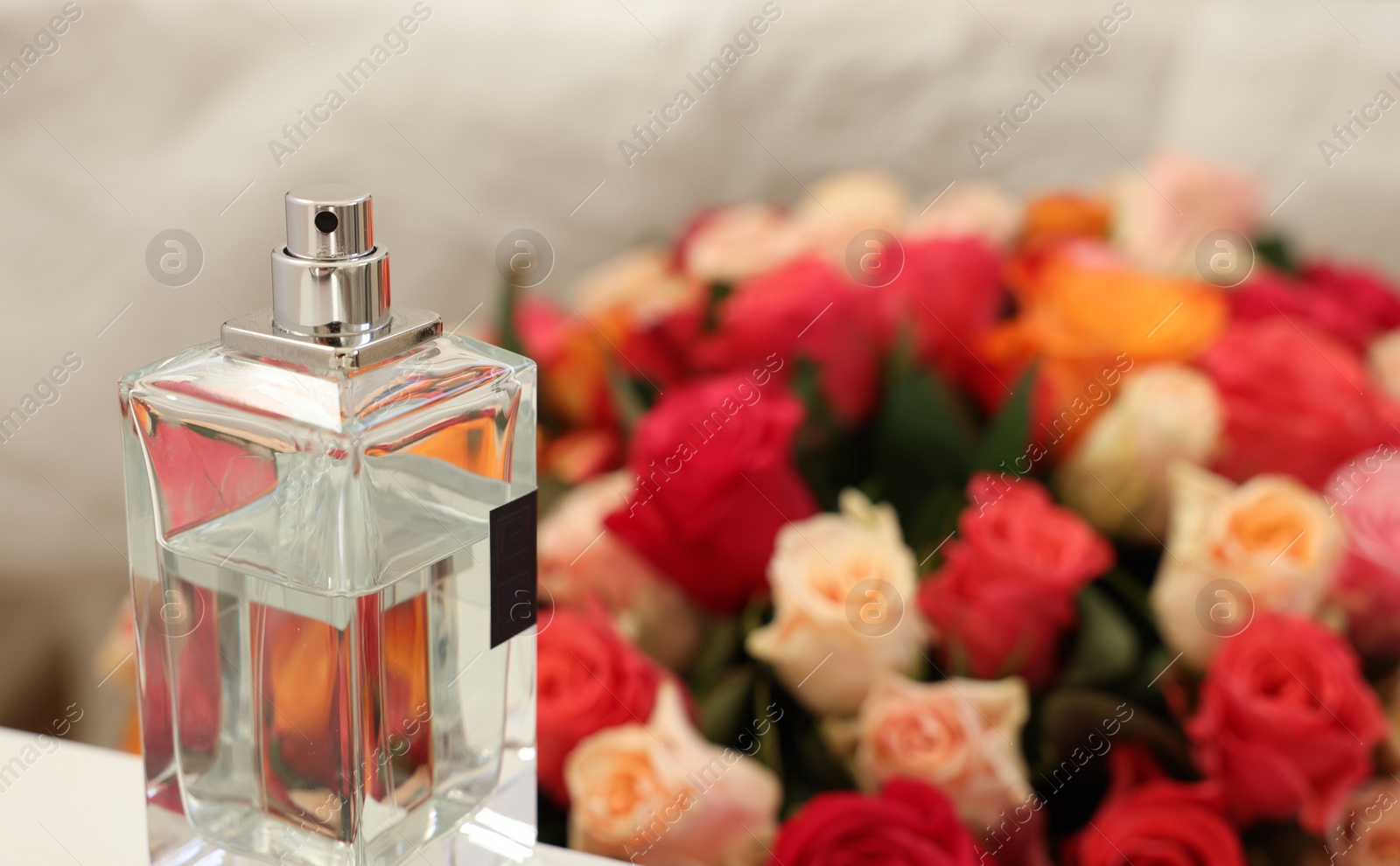 Photo of Bottle of perfume against bouquet of beautiful roses, closeup. Space for text