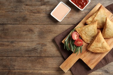 Photo of Fresh delicious crispy samosas served on wooden table, flat lay. Space for text