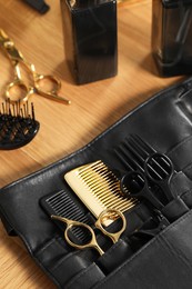 Hairdresser tools. Professional scissors and combs in leather organizer on wooden table, closeup