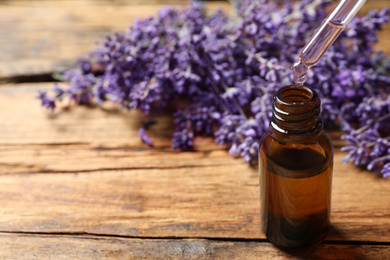 Photo of Dripping lavender essential oil into bottle on wooden background. Space for text