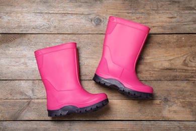 Pair of bright pink rubber boots on wooden background, top view