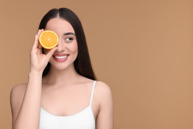 Beautiful young woman with piece of orange on beige background. Space for text