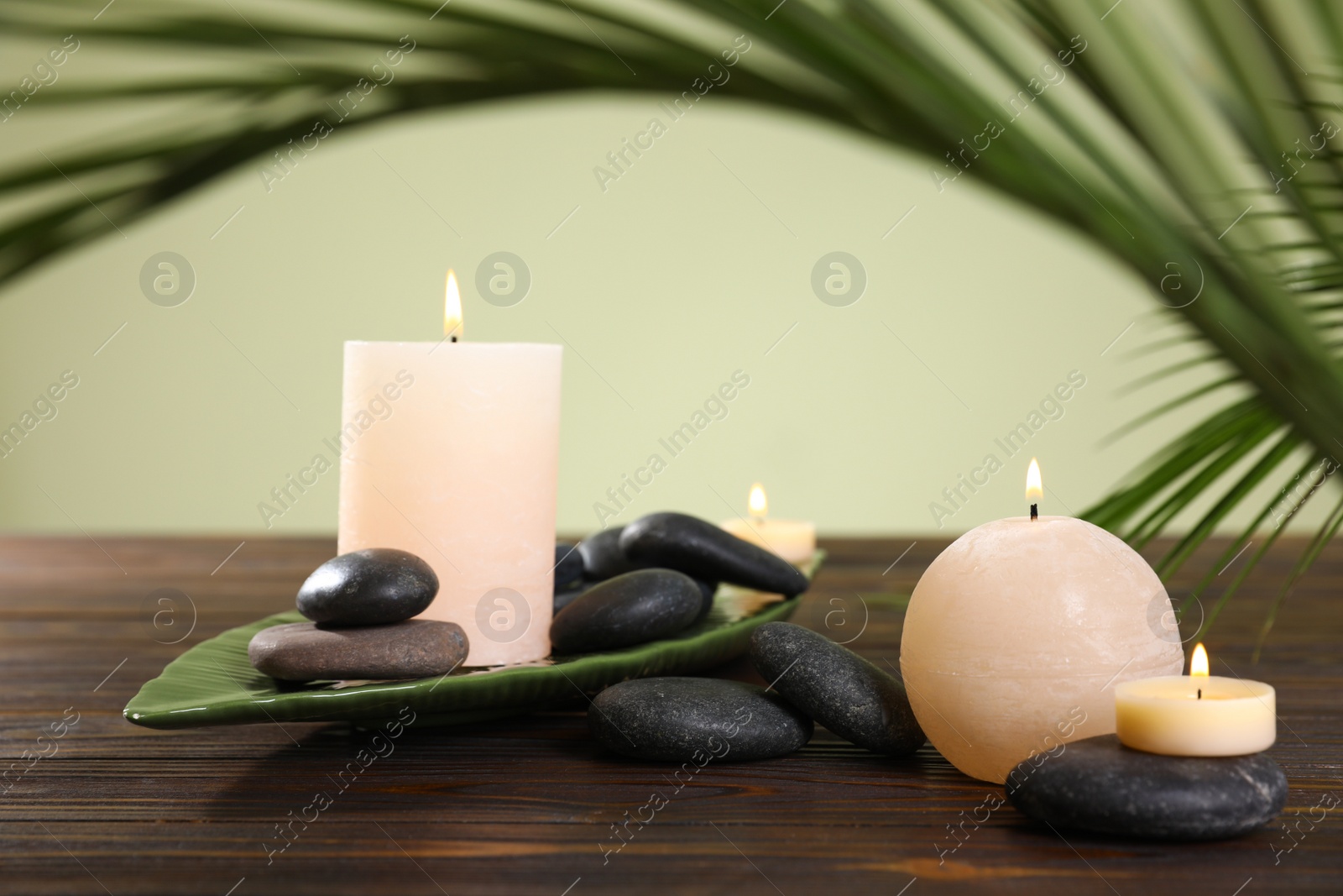 Photo of Composition of spa stones and burning candles on wooden table against light green background