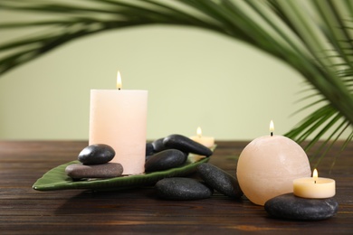 Composition of spa stones and burning candles on wooden table against light green background