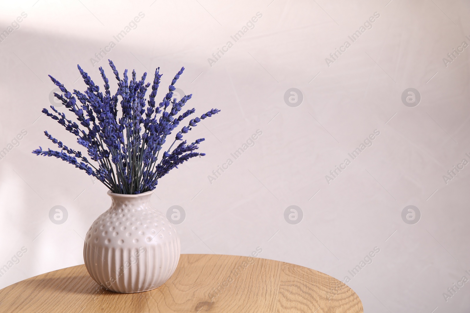 Photo of Bouquet of beautiful preserved lavender flowers on wooden table near beige wall, space for text