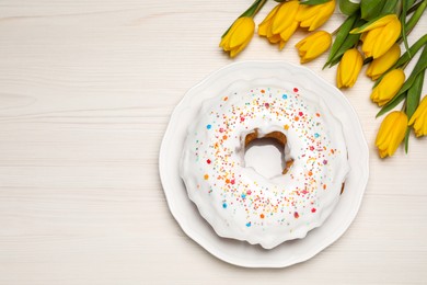 Photo of Easter cake with sprinkles and tulips on white wooden table, flat lay. Space for text