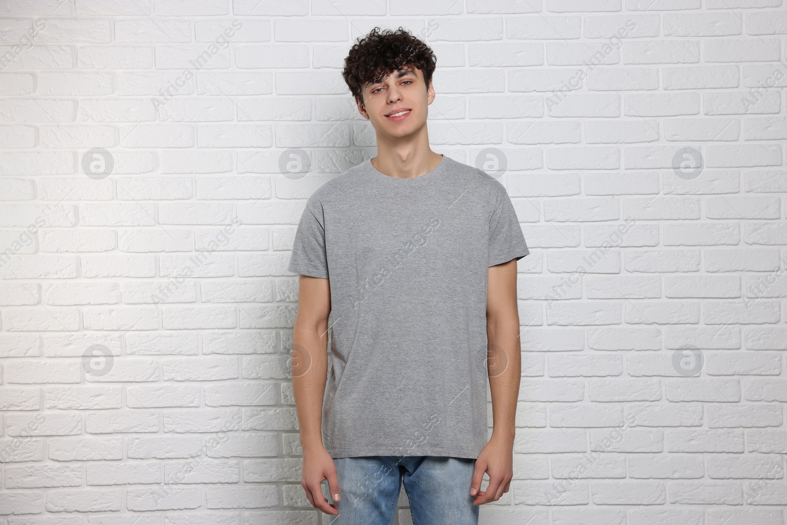 Photo of Man wearing gray t-shirt near white brick wall. Mockup for design