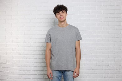 Photo of Man wearing gray t-shirt near white brick wall. Mockup for design