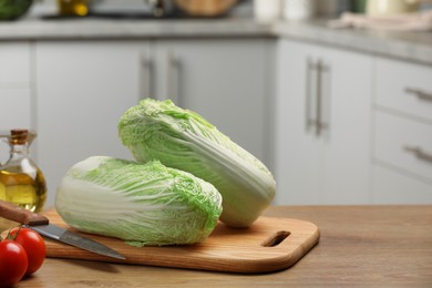 Photo of Fresh Chinese cabbages, knife, tomatoes and oil on wooden table in kitchen, space for text