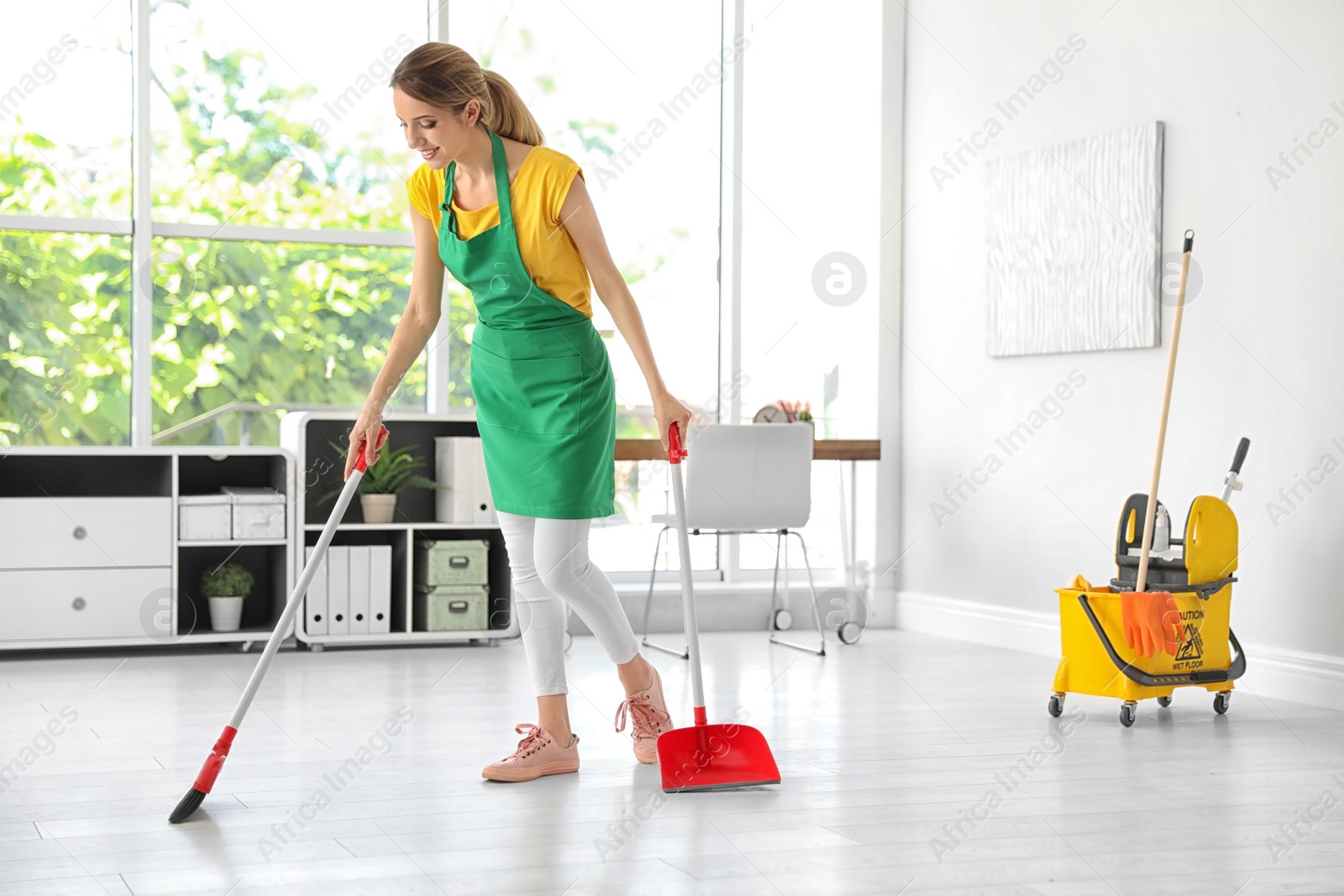 Photo of Young woman with broom and dustpan cleaning in office