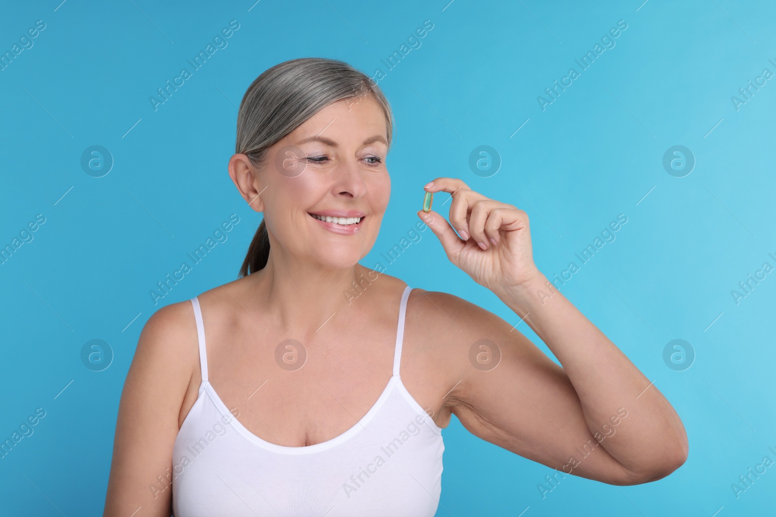 Photo of Beautiful woman with vitamin capsule on light blue background