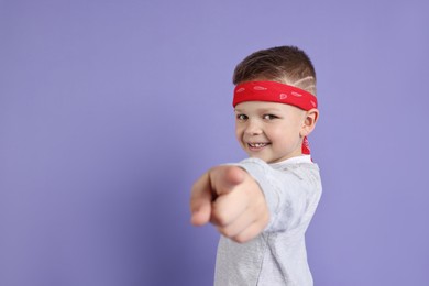 Happy little boy pointing at something on violet background. Space for text