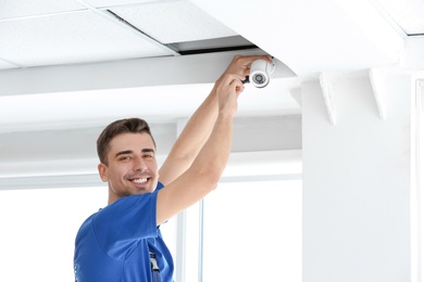 Photo of Technician installing CCTV camera on ceiling indoors