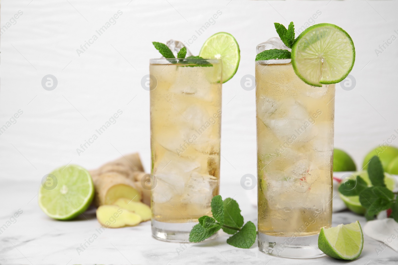 Photo of Glasses of tasty ginger ale with ice cubes and ingredients on white marble table