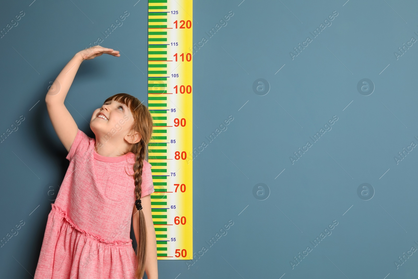 Photo of Little girl measuring her height on color background