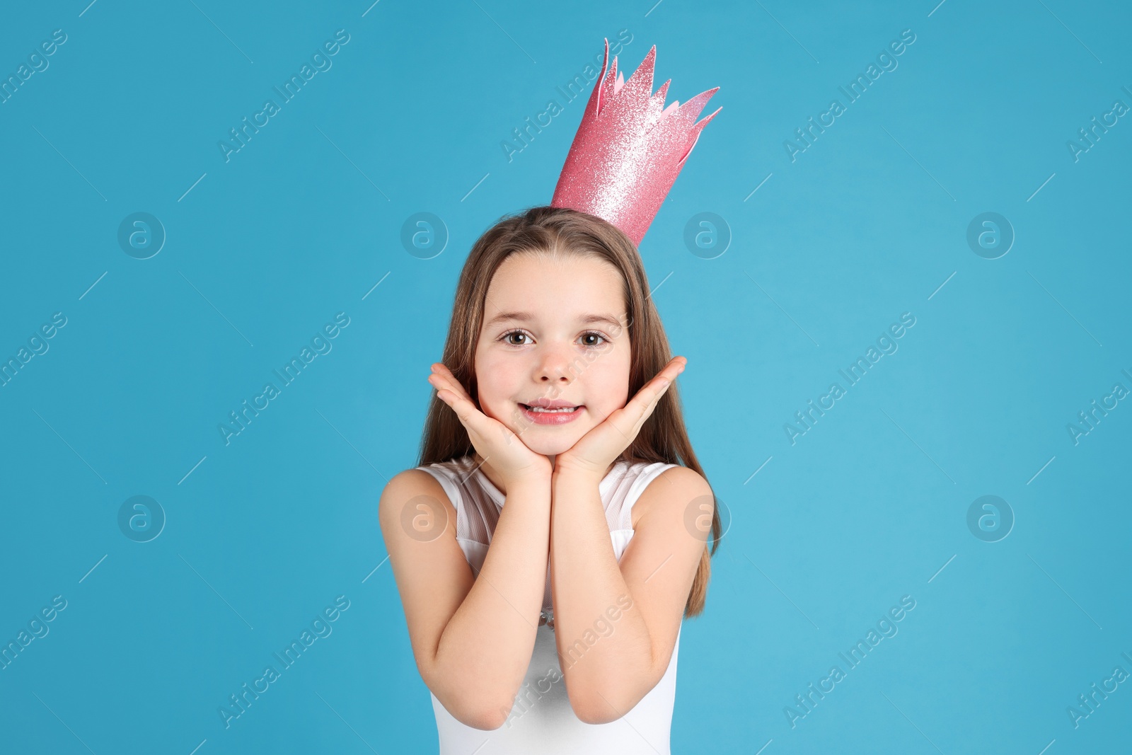 Photo of Cute girl in pink crown on light blue background. Little princess