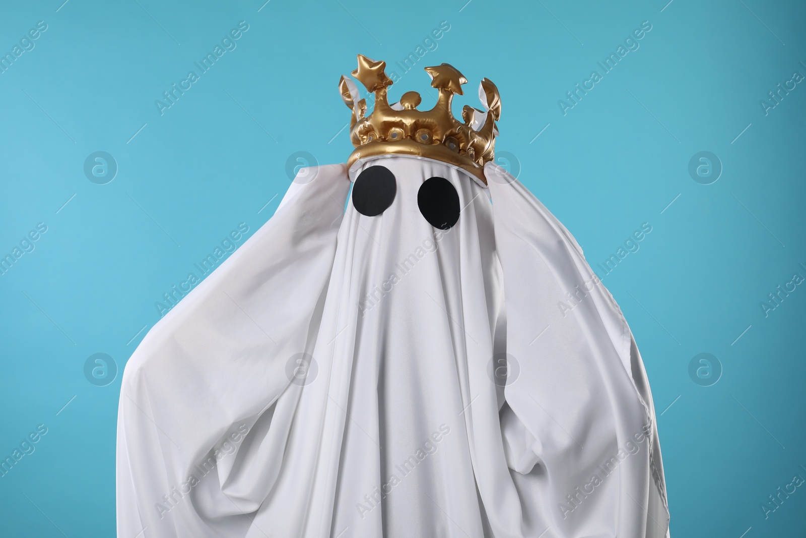 Photo of Person in ghost costume and luxurious crown on light blue background