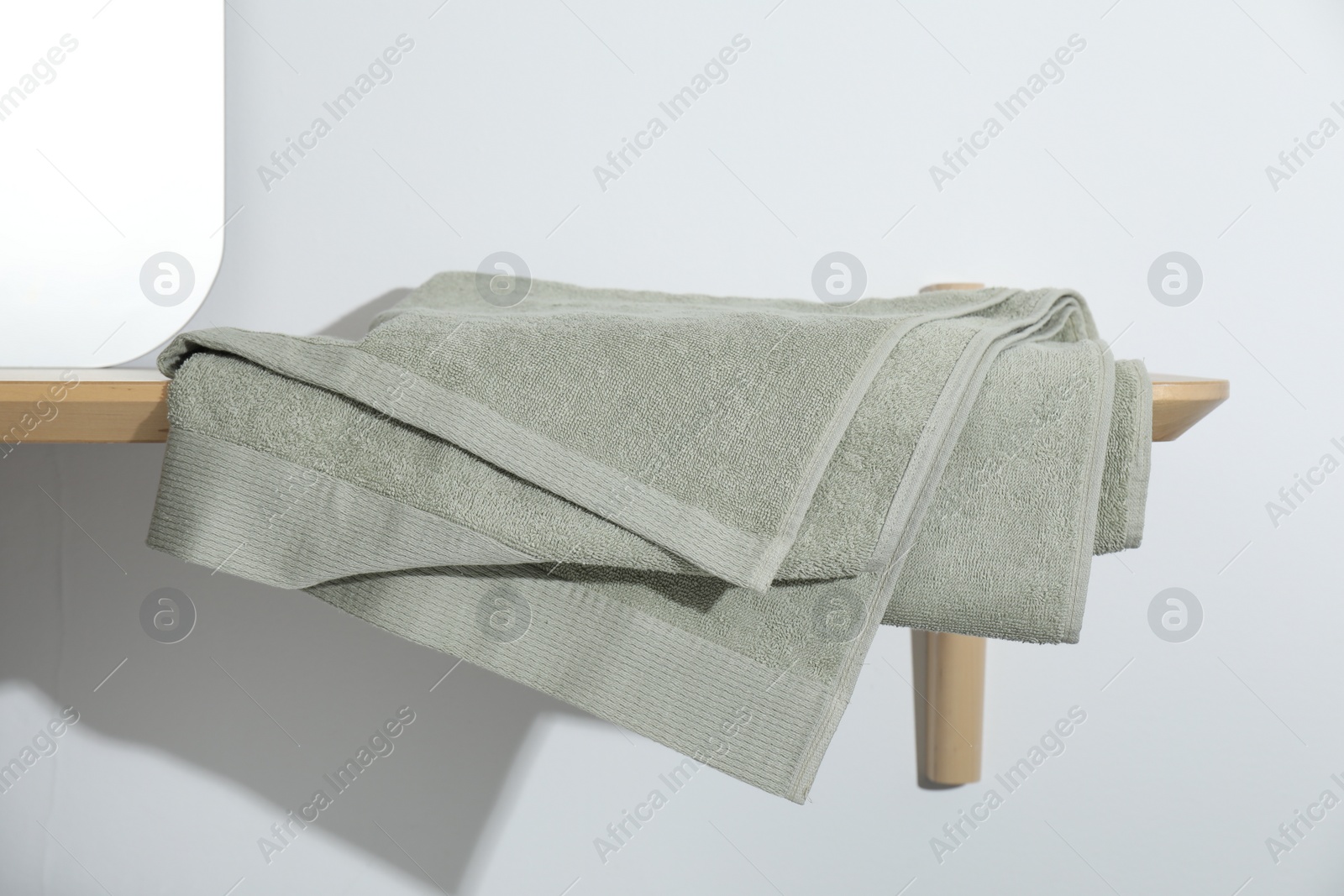 Photo of Green terry towel on wooden shelf near white wall
